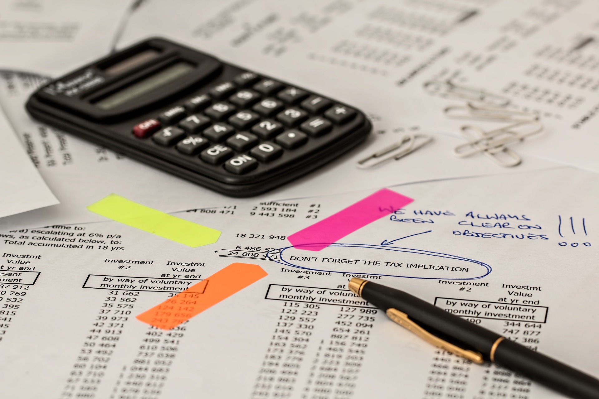 A close-up view of a desk covered with financial documents, a calculator, and a pen, highlighted with colorful markers emphasizing key figures and notes.
