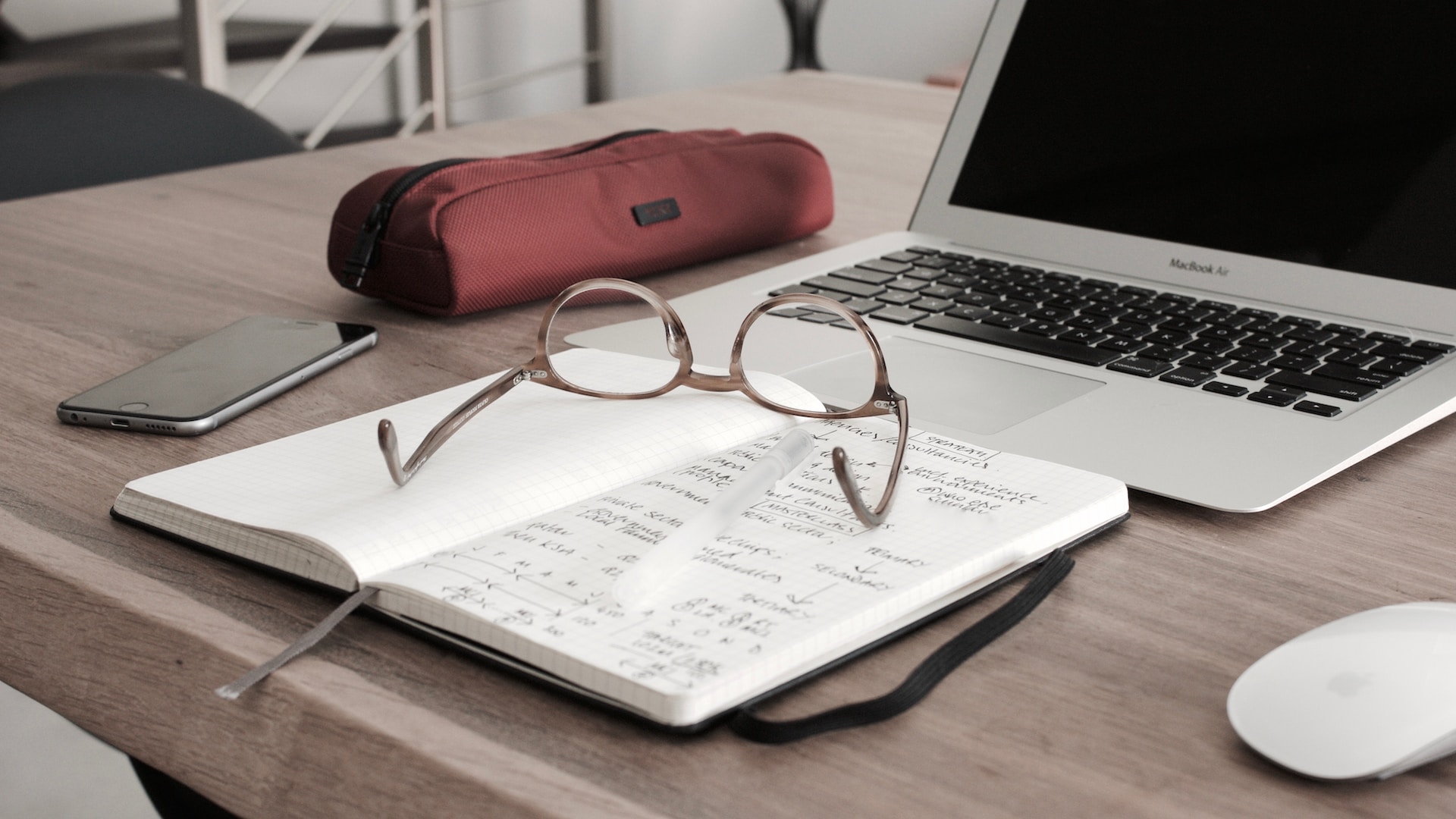 Reading Glasses on top of a working desk with a mouse and laptop beside