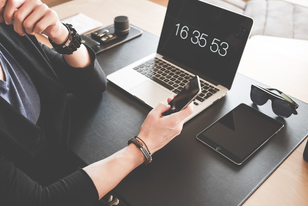 accountant checking her mobile phone while her laptop is showing the time