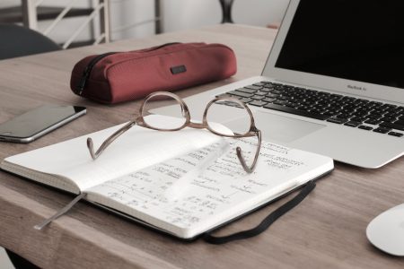 Reading Glasses on top of a working desk with a mouse and laptop beside
